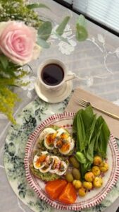Delicious breakfast featuring avocado toast, boiled eggs, fresh greens, and cup of tea.