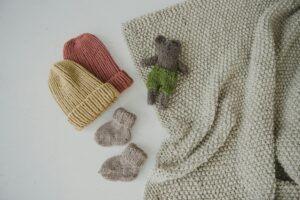 A collection of cozy handmade knitted items including beanies and a toy bear on a white surface.