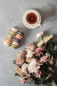 A top view of a tea cup, assorted macarons, and a flower bouquet on a textured surface.